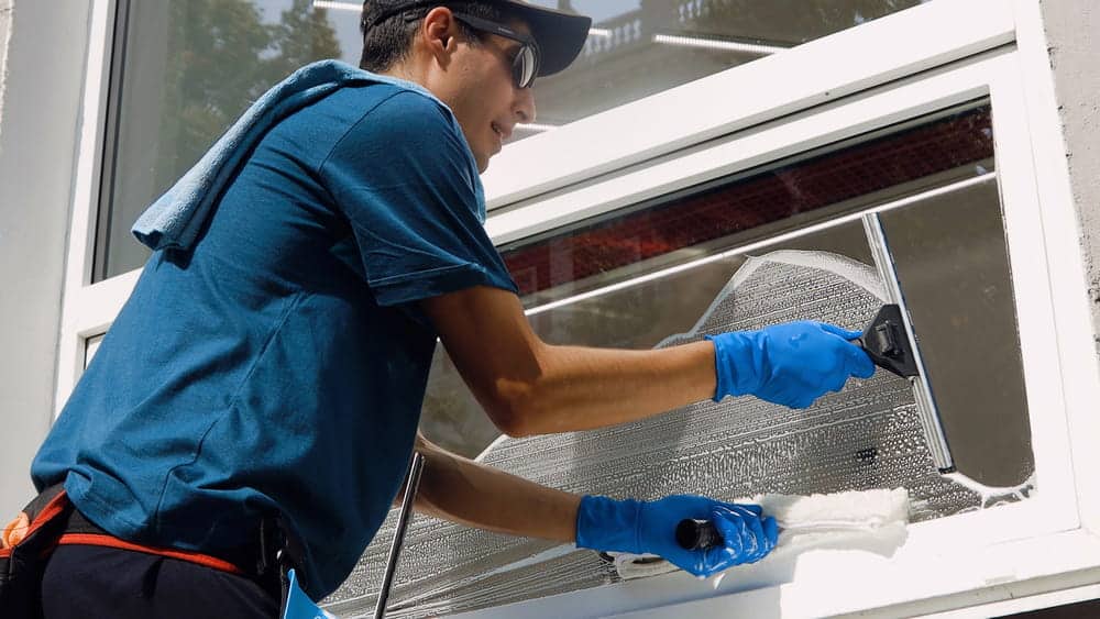 Male professional cleaning service worker in overalls cleans the windows and shop windows of a store with special equipment Male professional cleaning service worker in overalls cleans the windows and shop windows of a store with special equipment