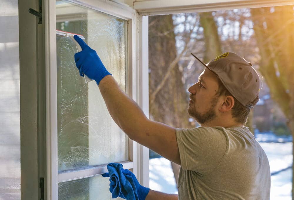 Young man is using a rag and squeegee while cleaning windows, professional window cleaner
